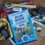 button collecting tools including a National Button Society Blue Book, wire brush, polishing cloth, mounting wire, caliper, hot needle, magnifying glass or loupe